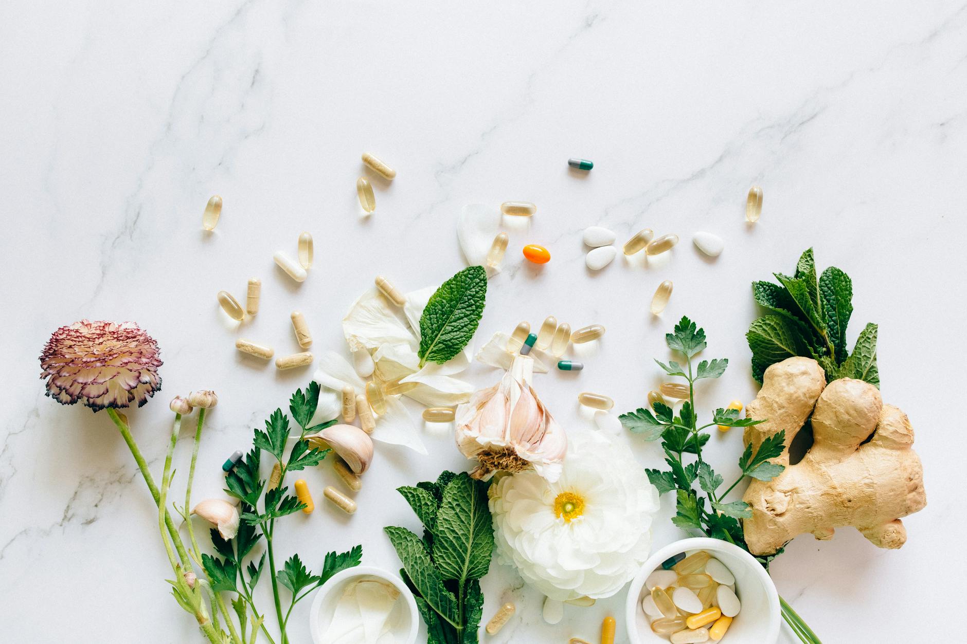 Supplements along with herbs, ginger root, flowers, garlic on a marbled counter, birds eye view