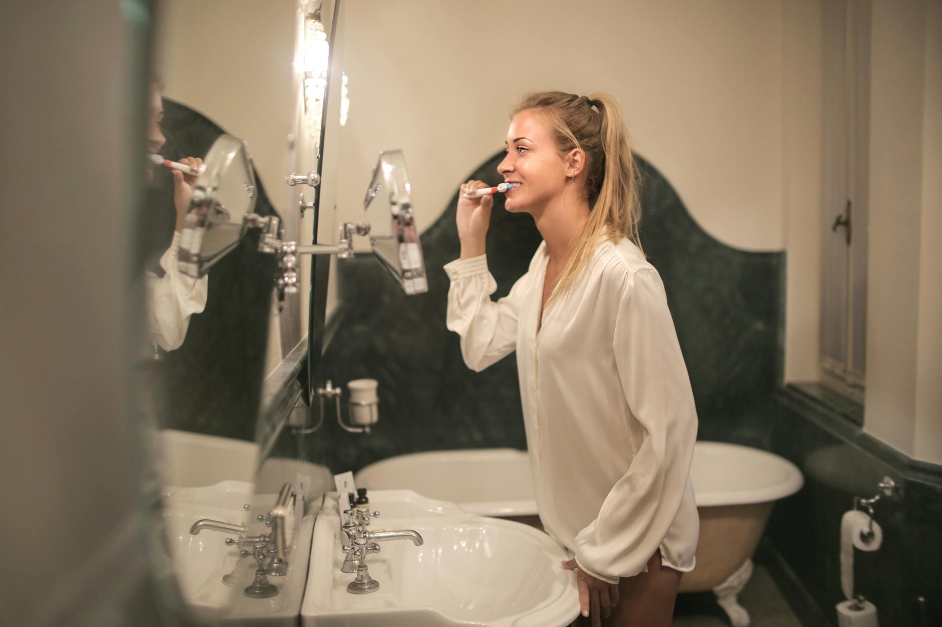 young woman cleaning teeth in bathroom to benefit physical health