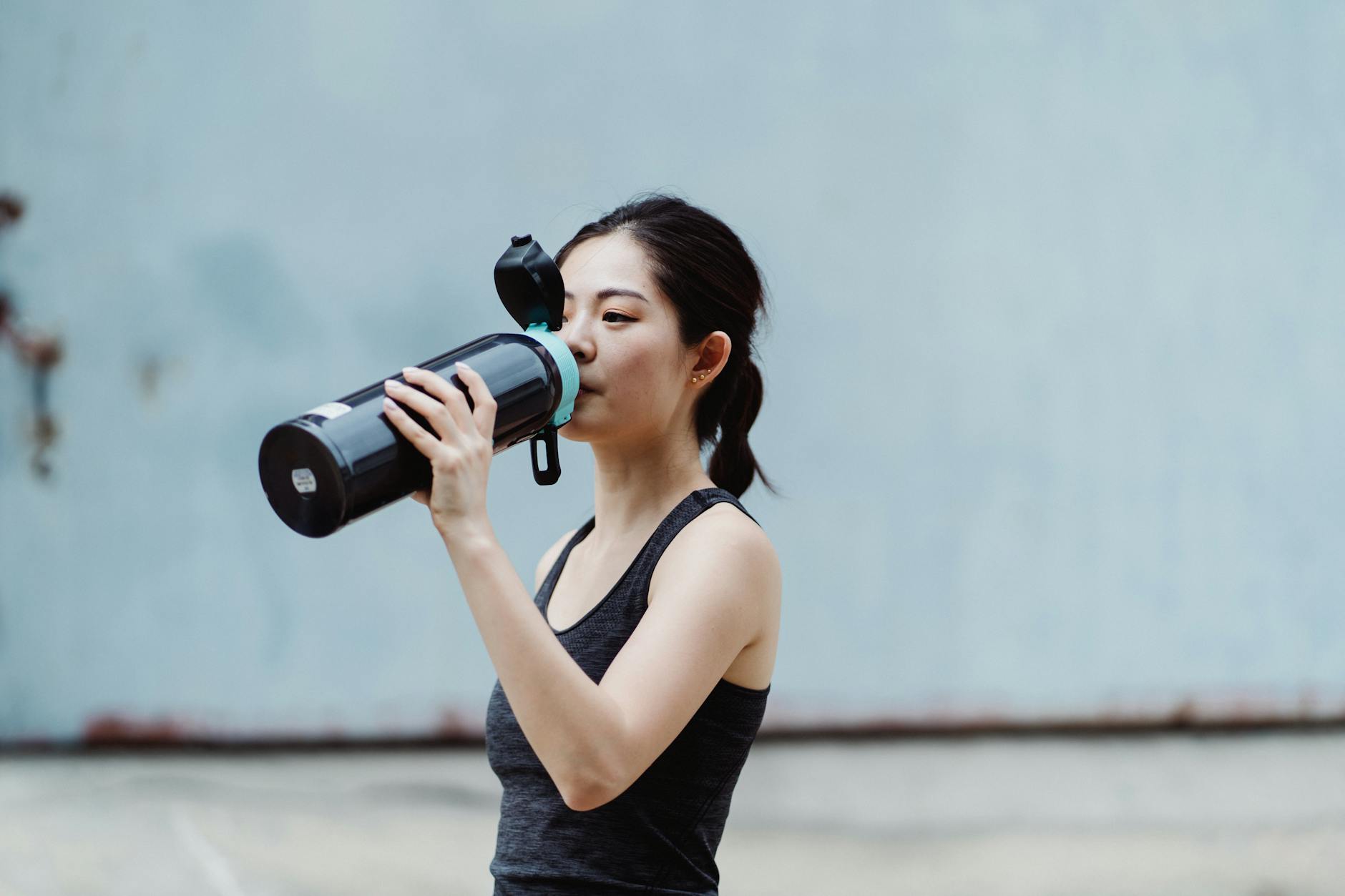 young woman drinking water from stainless steel tumbler to improve physical wellness