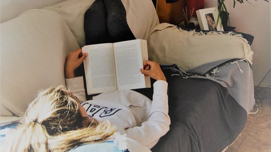 woman reading book while lying on sofa