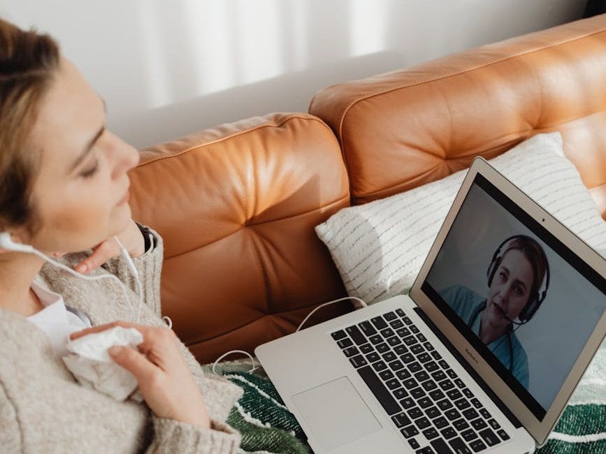 Woman on couch with laptop on lap on zoom call for Health Coahcing.