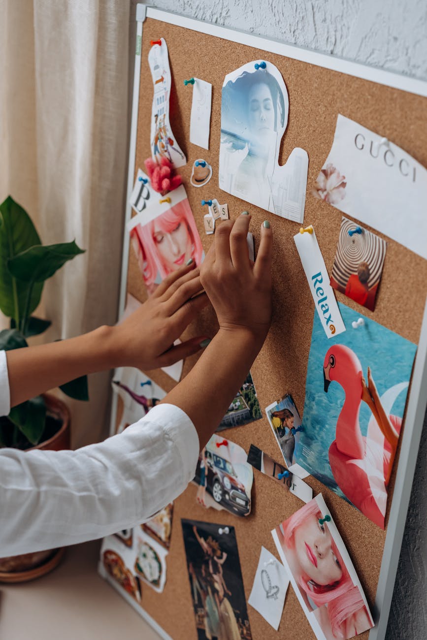 a hand sticking cut out magazine on a cork board for a vision board.